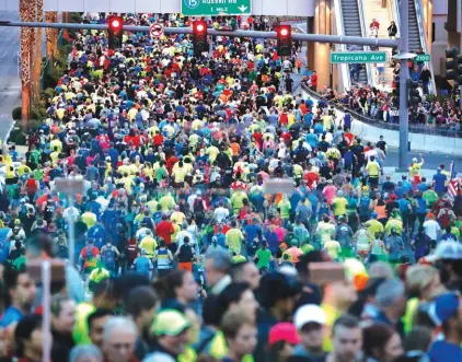  ??  ?? People run along the Las Vegas Strip as people walk across a pedestrian bridge during the Rock ‘n’ Roll Las Vegas Marathon Photo: AP