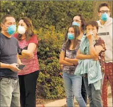  ?? Mel Melcon Los Angeles Times ?? SHIELDING their noses from the smoky air, Carpinteri­a residents monitor the Thomas fire from Santa Monica Road on Monday.