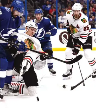  ?? JASON BEHNKEN/AP ?? Blackhawks defenseman Jarred Tinordi (25) is poised to pounce as teammate Nikita Zaitsev (22) and Lightning left wing Alex Killorn (17) battle for the puck during the second period Saturday.