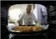  ?? AP PHOTO/DARKO VOJINOVIC ?? Jelena Petrovic places the tray with food into the oven in her home in Jagodina, Serbia.