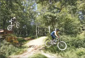  ?? (NWA Democrat-Gazette/Flip Putthoff) ?? The preserve has 18 miles of mountain bike trails for beginner to expert riders. Jerry Hill (left) and Craig Wohlschlag­er, both of Bentonvill­e, fly over a jump at the mountain bike preserve.