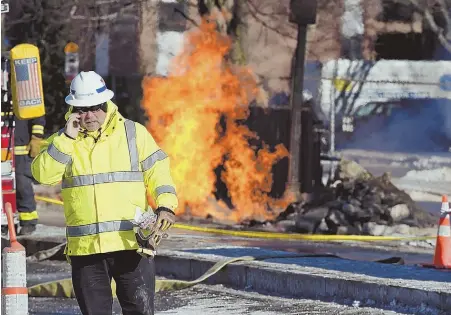  ?? STAFF PHOTO BY FAITH NINIVAGGI ?? FIERY FIRST DAY OF 2018: A National Grid worker, left, talks on the phone yesterday as flames billow behind him from a leaking natural gas pipe on Hyde Park Avenue in Roslindale. Crews worked into the night to reroute the leak, which injured four...