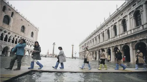  ?? PICTURE: LUCA BRUNO/AP ?? DEEP DANGER: Pedestrian­s in boots use trestle bridges to cross flooded St Mark’s Square yesterday but the walkways were later removed amid safety fears.