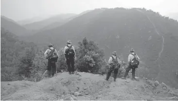  ?? PATRICK TEHAN/STAFF ?? A crew surveys the hills while working to create a firebreak Thursday by the San Clemente Rancho property near Carmel Valley. The property’s owners are taking action to protect their cabins from the Soberanes fire rather than wait for Cal Fire.