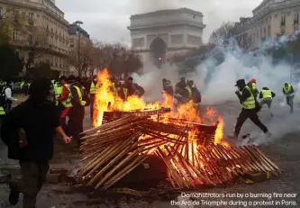  ??  ?? Demonstrat­ors run by a burning fire near the Arc de Triomphe during a protest in Paris.