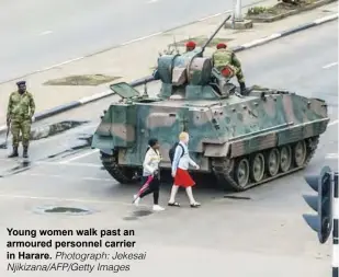  ?? PIthowtaos­graat pth:isJepkoein­statihat Njikizana/AFP/Getty Images ?? Y o ugng women walk past an armtooured personnel carrier