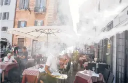  ?? RICCARDO DE LUCA/AP ?? A fan sprays mist as customers sit outside a cafe during a heat wave last July in downtown Rome. The temperatur­e that day reached 104 degrees.