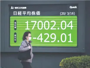  ?? AFP ?? A woman walks past a quotation board displaying share price closing numbers of the Tokyo Stock Exchange in Tokyo yesterday.
