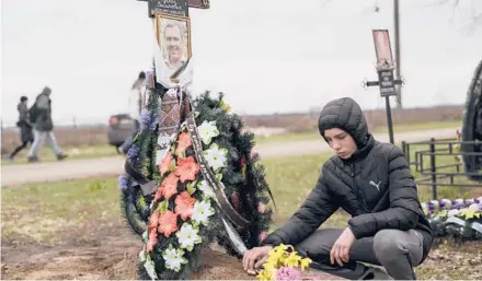  ?? PETROS GIANNAKOUR­IS/AP ?? Yura Nechyporen­ko at the grave of his father, Ruslan, in Bucha. Ruslan was killed and Yura was wounded by a Russian soldier.