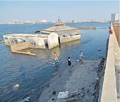  ??  ?? Children play next to an abandoned mosque that stands beyond the seawall in the Muara Baru area in Jakarta