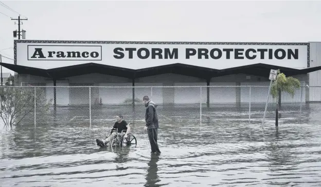  ?? PICTURE: BRENDAN SMIALOWSKI/ AFP/GETTY IMAGES ?? 0 Brad Matheney offers to help a man in a wheelchair in a flooded street after Hurricane Henry had passed through Galveston