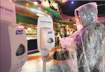  ?? ALLEN J. SCHABEN Los Angeles Times ?? A DISNEYLAND guest uses a new hand sanitizer before ordering food at the park on a rainy Thursday. Disneyland and Disneyland California Adventure will close Saturday morning through the end of the month.