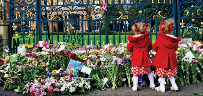  ?? ?? MATCHING COLOURS: Two-year-old twins Abigail and Arabella Glen pay their respects surrounded by a mountain of blooms left by mourners at the gates of Hillsborou­gh Castle in Co. Down