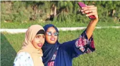  ??  ?? Rahma Abdullahi Mohamud (right) and Hani Hussein take selfies pictures with a mobile phone, after buying clothes designed by fashion designer Muna Mohamed Abdullahi, at Peace Garden in Mogadishu, Somalia.