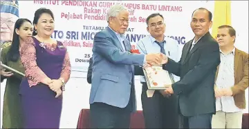  ??  ?? Manyin (left) presents a certificat­e of attendance to a participan­t of the education colloquium at Serian Civic Centre.