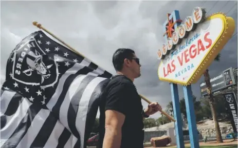  ??  ?? Fan Matt Gutierrez carries a Raiders flag Monday by a famous sign welcoming visitors to Las Vegas. NFL team owners approved the move of the Oakland franchise to the largest city in Nevada in a vote in Phoenix. John Locher, The Associated Press