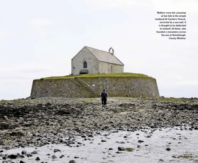  ??  ?? Walkers cross the causeway at low tide to the simple medieval St Cwyfan’s Church, encircled by a sea wall. It is thought to be dedicated to Ireland’s St Kevin, who founded a monastery across the sea at Glendaloug­h, County Wicklow.