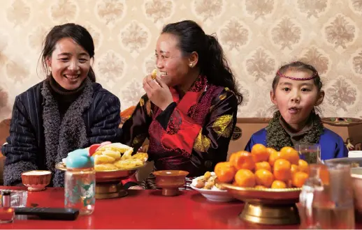  ??  ?? Nyidron (center) eats Kasai, a traditiona­l Tibetan pastry for the New Year, at home in downtown Lhasa. — Xinhua