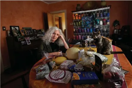  ?? Associated Press ?? ■ Phyllis Marder poses with her cat, Nellie, on Nov. 5 with food she recently obtained from a local food bank in the dining room of her home in Evanston, Ill. At first, Marder, 66, didn’t tell anyone about going to food pantries. Then she had a change of heart. “Keeping a secret makes things get worse,” she says ’”… and makes me feel worse about myself, and so I decided that it was more important to talk about it.”