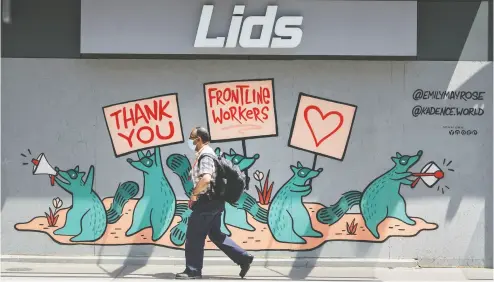  ?? Peter J. Thompson / financial Post ?? A pedestrian in a mask walks past a mural of support for frontline workers on a boarded-up storefront in Toronto. Statistics Canada estimates the Canadian economy contracted 11 per cent in April as businesses were shuttered.