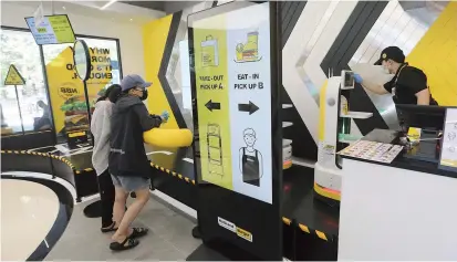  ??  ?? An employee (right) controls a robot to deliver a takeout bag with food to a customer at No Brand Burger in Seoul, South Korea. These robotic services, without a single face-to-face interactio­n, have been seen as a selling point amid the coronaviru­s pandemic and its restrictio­ns.