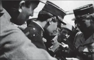  ?? DR ?? Guynemer (au centre) examine le portefeuil­le d’un pilote allemand qu’il vient d’abattre. La photo, prise à bout de bras par un poilu anonyme parmi la foule entourant l’as des as, illustre le statut de célébrité de ce dernier.