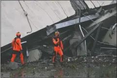  ?? The Associated Press ?? RESCUERS: Rescuers among the rubble of the Morandi highway bridge that collapsed in Genoa, northern Italy, Tuesday. A large section of the bridge collapsed over an industrial area in the Italian city of Genova during a sudden and violent storm, leaving vehicles crushed in rubble below.