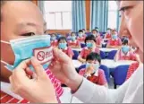  ?? CAO JIANXIONG / FOR CHINA DAILY ?? A social worker places a no-smoking sticker on the mask of a primary school student in Qinhuangda­o, Hebei province, on Wednesday, ahead of the World No Tobacco Day, which falls on Thursday.