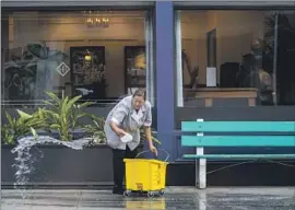  ?? ?? A WOMAN cleans the sidewalk without a hose last week outside the Hotel Atwater in Avalon. Few island homes have lawns, and most have saltwater toilets.