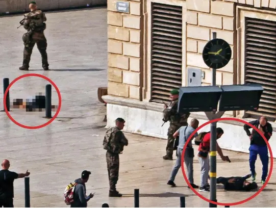  ??  ?? Carnage: A policeman points his gun at the dying attacker, circled right, as soldiers guard the body of one victim, circled left