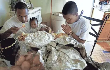  ?? ?? Nov. 25, 2009: Cherry Adams prays over Thanksgivi­ng dinner with Terrence Rainey, left, and his son Ta'derius, 7 months, that was provided by Youth Villages counselors.