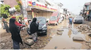  ?? Photo / AP ?? Indonesia residents walk near the wreckage of vehicles that were swept away by floodwater­s.