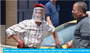  ?? — AFP ?? TUNIS: A Tunisian man wearing protective gear amid the COVID-19 pandemic looks on as he chats with another person on a street in the Kram area of the capital on May 8, 2020.