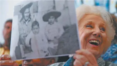  ??  ?? President of the Grandmothe­rs of Plaza de Mayo, Estela de Carlotto, holds a photo of Rosario del Carmen Ramos, pictured with two of her three sons Ismael, right, and Camilo, before she disappeare­d.