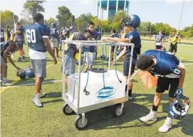  ?? BRIAN KRISTA/BALTIMORE SUN MEDIA GROUP ?? Players gather around the water tank at Howard High on Wednesday. Since 1995, 47 high school football players in the United States have died from heatstroke.