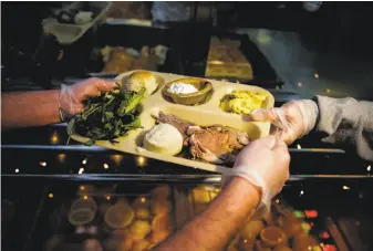  ?? Gabrielle Lurie / The Chronicle 2017 ?? Volunteer Kai Lord (right) hands a tray to another volunteer during a 2017 Christmas Eve free lunch at Glide Memorial United Methodist Church hosted by House of Prime Rib in S.F.