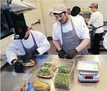  ?? ELAINE THOMPSON / THE ASSOCIATED PRESS FILES ?? Workers make sandwiches in an Amazon Go store in Seattle. The company is boosting its minimum wage for all U.S. workers to $15 per hour starting next month, a move that will benefit more than 350,000 workers.