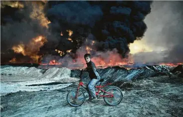  ?? Carl Court / Getty Images ?? A boy pauses on his bike as he passes an oil field that was set on fire by retreating ISIS fighters ahead of the Mosul offensive Friday in Qayyarah, Iraq. ISIS has forced families to leave their homes for Mosul.