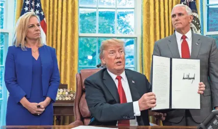  ??  ?? President Donald Trump, flanked by Homeland Security Secretary Kirstjen Nielsen and Vice President Mike Pence, holds an order he signed Wednesday to stop migrant children from being separated from their parents.