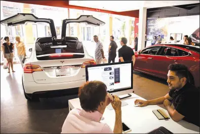  ?? Bloomberg News file photo ?? An employee speaks with a customer at the Tesla Inc. showroom in Newport Beach, Calif., earlier this month. Tesla’s finances rather than its cars were the focus Monday after a report that the company asked suppliers for refunds to help it turn a profit.