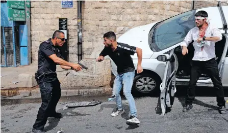  ??  ?? AN ISRAELI policeman raises his gun at a Palestinia­n man next to a wounded Orthodox Jewish man who crashed his car near the Lions’ Gate, as clashes continue at the Temple Mount in the old city of Jerusalem, yesterday. | EPA