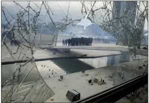  ?? (AP/Eraldo Peres) ?? Police stand on the other side of a window at Planalto Palace that was shattered by supporters of Brazil’s former President Jair Bolsonaro, after they stormed the official workplace of President Luiz Inacio Lula da Silva, on Jan. 8 in Brasilia, Brazil.