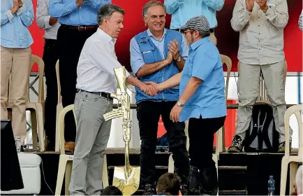  ?? PHOTO: REUTERS ?? Jean Arnault, head of the United Nations Mission to Colombia, applauds as Colombian President Juan Manuel Santos, left, and FARC leader Rodrigo Londono shake hands at the disarmamen­t ceremony in Mesetas.