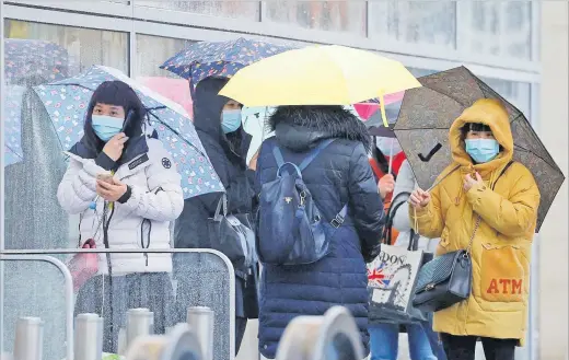  ?? People wearing face masks shelter under umbrellas outside a department store following the outbreak of the coronaviru­s disease (COVID-19) in Manchester, Britain. Picture: REUTERS ??