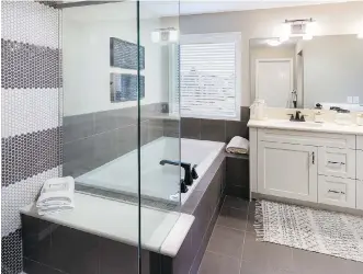  ??  ?? The ensuite boasts dual vanities under a full-width mirror, a deep soaker tub, and glass-encased shower.