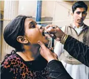  ?? SARAH CARON/FOR THE WASHINGTON POST ?? Hafsa Ali, 10, receives anti-polio drops from Shehnaz Bibi, a volunteer who goes door-to-door to administer the vaccine.