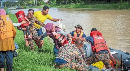  ?? ?? On dry land: Fire and rescue unit members helping a family from Kampung Sri tanjung that was trapped by rising flood waters. — bernama