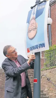  ?? FOTO: JÜRGEN LAASER ?? Ralf Derichs (SPD) hofft, dass ihm das auf dem Kopf stehende Wahlplakat vor der Sankt-Peter-und-Paul-Kirche in Wegberg Glück bringt.