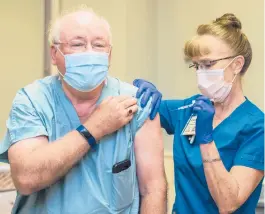  ?? MICHAEL HOLAHAN/THE AUGUSTA CHRONICLE ?? Registered nurse Candy Russell gives Dr. William Kitchens a shot of the Pfizer COVID-19 vaccine Tuesday in Augusta, Georgia. Some states are again calling in medical personnel to help handle a surge of virus cases.