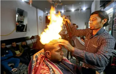  ?? PHOTO:REUTERS ?? Palestinia­n barber Ramadan Odwan styles the hair of a customer with fire at his salon in Rafah, in the Gaza Strip.